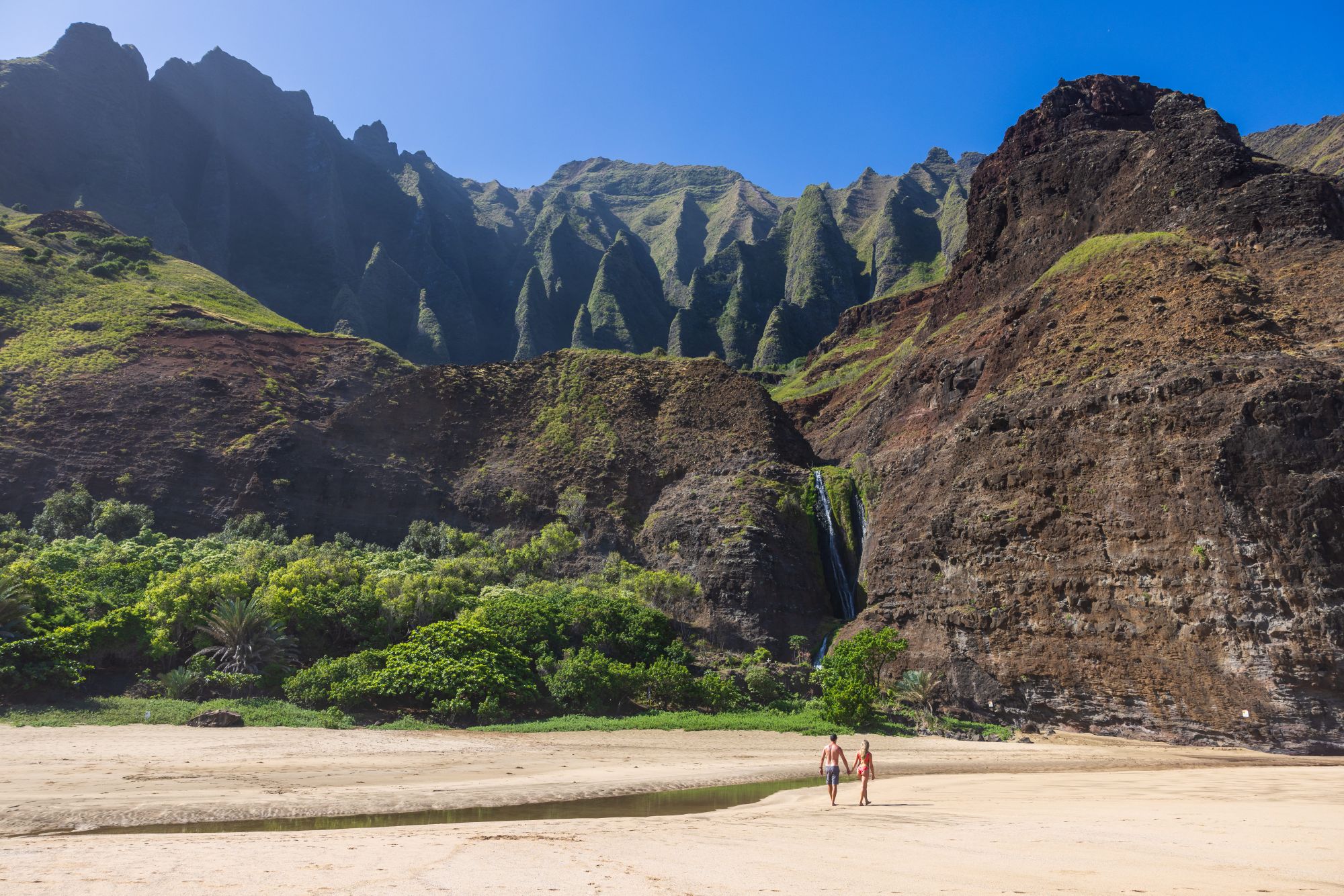 Una coppia cammina sulla spiaggia di Kalalau alle Hawaii tra scogliere e vegetazione